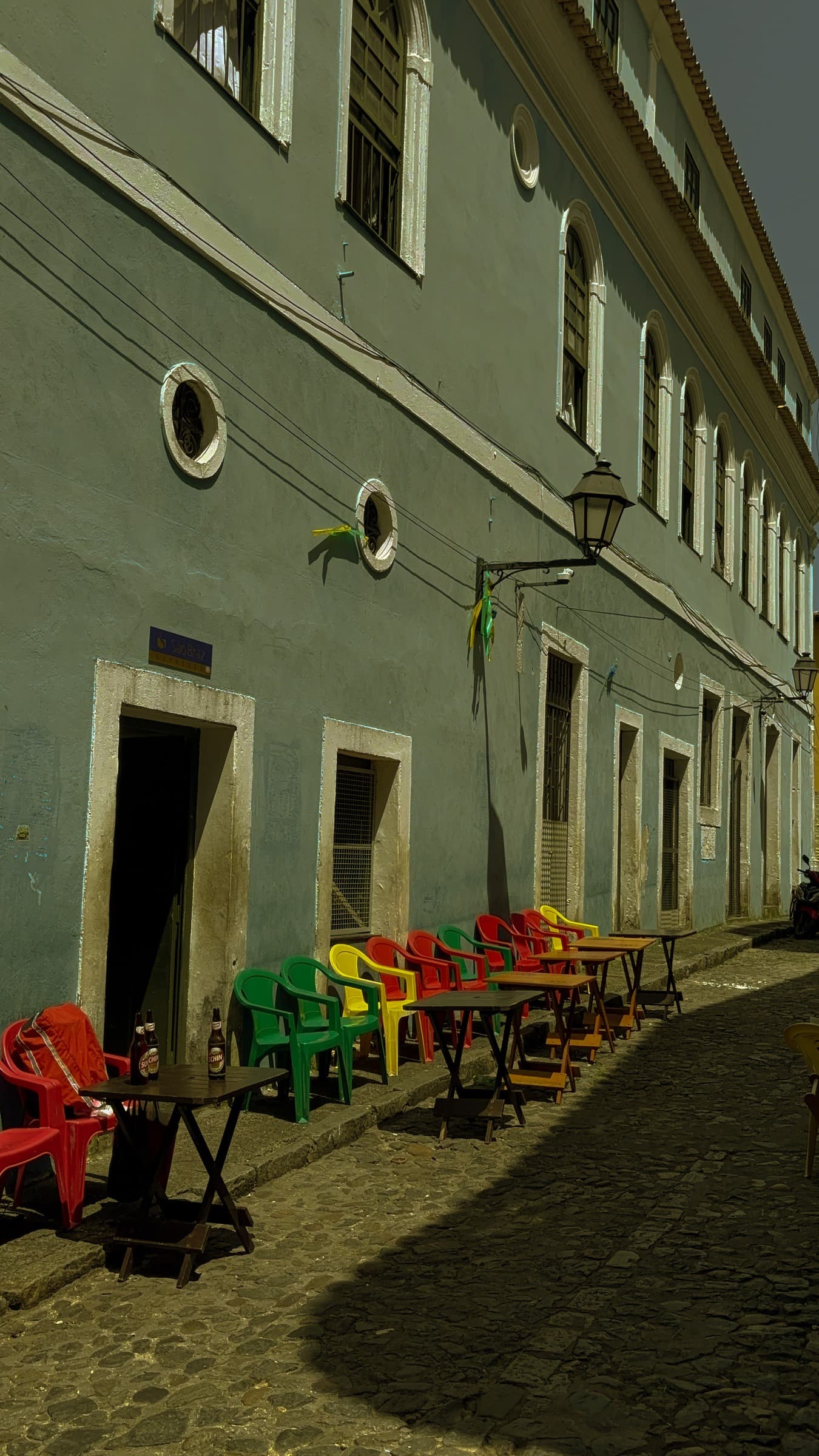 Rua de pedras no Pelourinho com fachada histórica, mesas e cadeiras coloridas.
