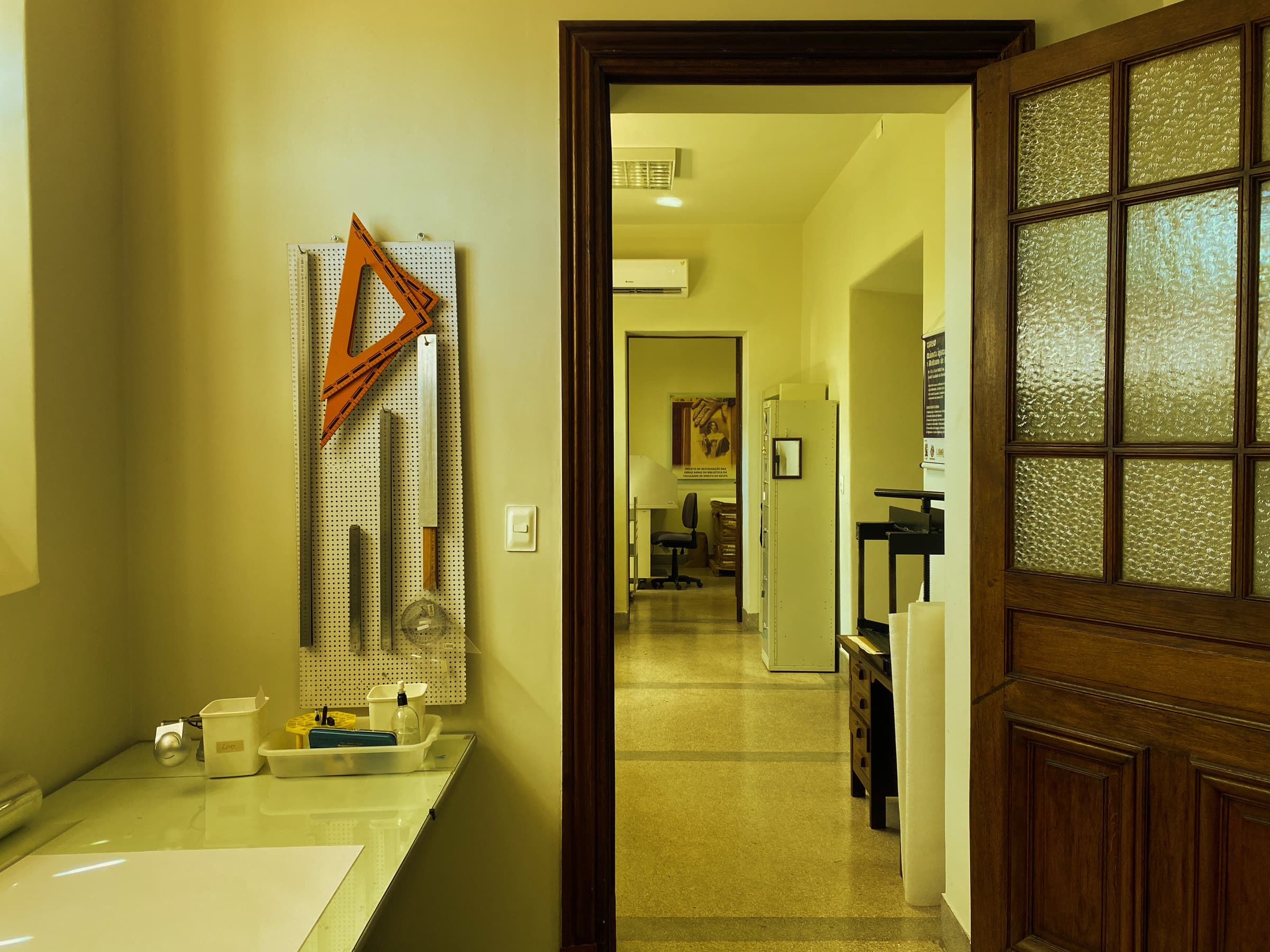 Sala de acervo com instrumentos de desenho, portas de madeira e armários ao fundo.
